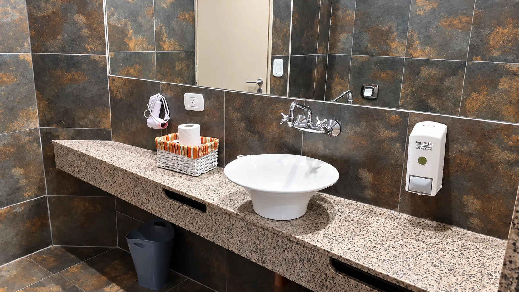 Lavabo blanco sobre mesada de granito, espejo y revestimiento oscuro
